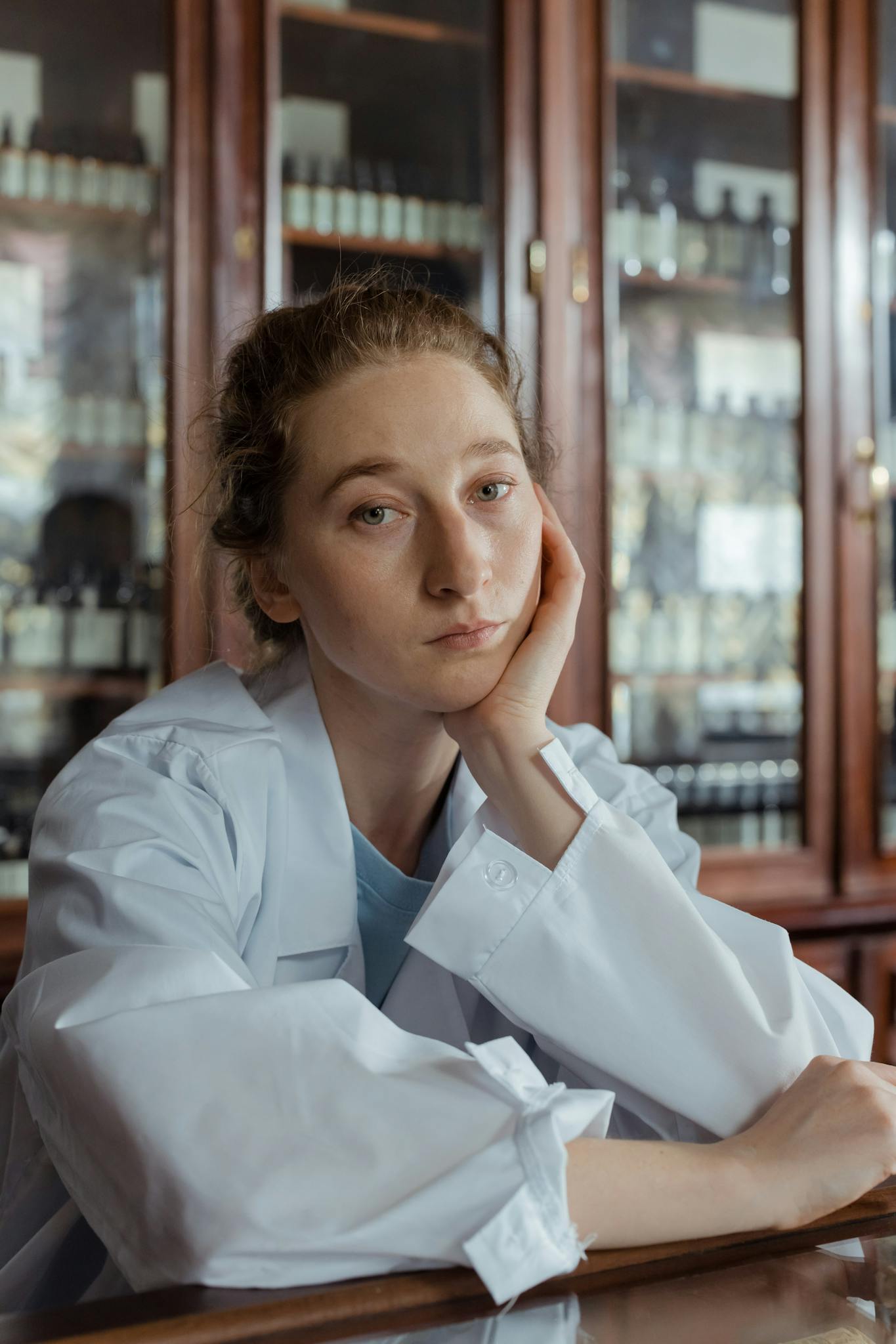 A thoughtful female pharmacist in a white coat sitting in a pharmacy.