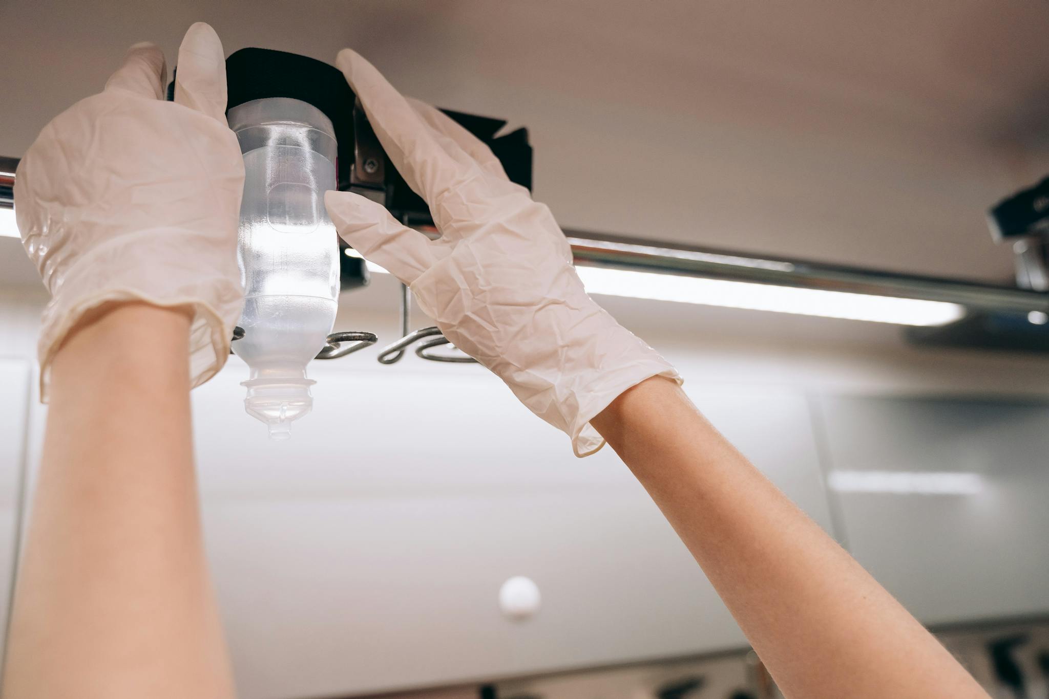 Close-up of gloved hands adjusting an IV drip in a clinical setting, emphasizing healthcare professionalism.